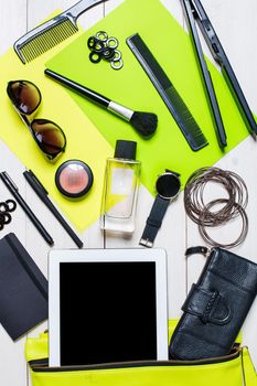 Flat lay, top view, mock up cosmetics and women's accessories fell out of the green handbag on white background. Phone, watch, pen, purse, curling