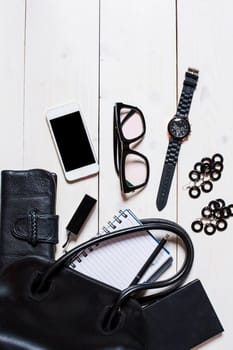 Flat lay, top view, mock up women's accessories fell out of the black handbag on white background. Phone, glasses, watch, notebook