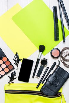 Flat lay, top view, mock up cosmetics and women's accessories fell out of the green handbag on white background. Phone, watch, pen, purse, curling