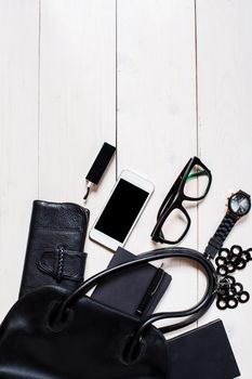 Flat lay, top view, mock up women's accessories fell out of the black handbag on white background. Phone, glasses, watch, notebook