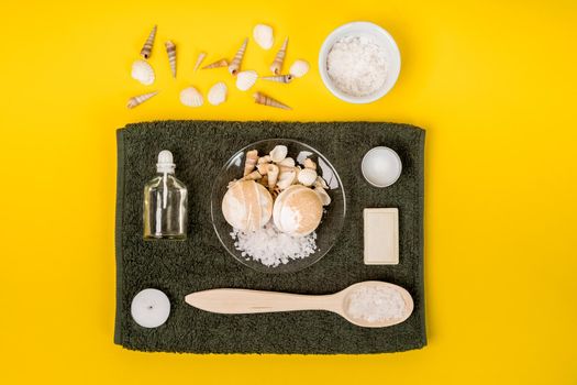 Spa set: soap, essential oil, sea salt and towel on a yellow background. Still life. Copy space