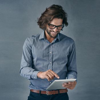 Shot of a handsome young man using a digital tablet against a gray background.