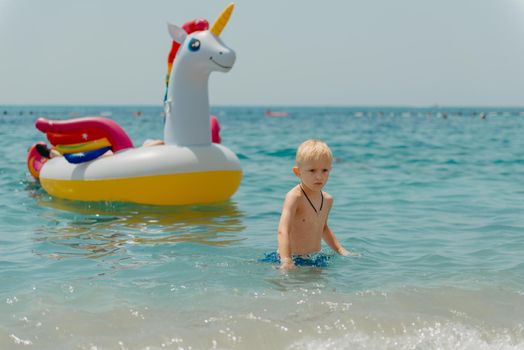 Child learning to swim in the open sea of tropical resort. Kids learn swimming. Exercise and training for young children. Little boy with colorful float board in sport club. Swimming baby or toddler. Happy child boy swims in sea in swimming circle with splash. Blue sky and water. Swimming training. Fun joy activities on vacation in the beach. Childhood moments lifestyle. Freedom careless. boy swim in the sea.