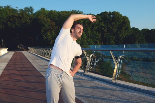 Handsome middle-aged Caucasian man, sportsman, athlete exercising outdoor, standing on a treadmill, warming up his body, stretching it before morning jog. Sport, active and healthy lifestyle conept
