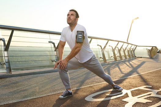 Young jogger sportsman preparing for the training. Athlete performing lunges, stretching his legs and warming up for running. Fitness and exercising. Keep your body fit