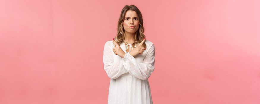 Beauty, fashion and women concept. Portrait of troubled blond girl in white dress need advice, trying make choice, smirk and frown puzzled, pointing left and right two variants, pink background.