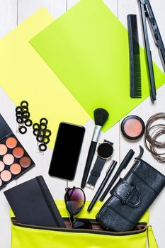 Flat lay, top view, mock up cosmetics and women's accessories fell out of the green handbag on white background. Phone, watch, pen, purse, curling