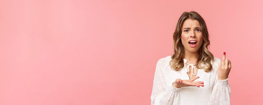 Close-up portrait of frustrated pissed-off, complaining beautiful girl tired of waiting for proposal, pointing at ring finger with bothered grimace, standing pink background disappointed.