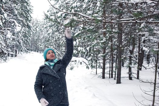 A happy woman in a winter snow-covered forest, holding a pine branch, shaking off the snow