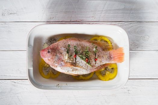 raw pink tilapia fish with vegetables in a baking dish, hands spice on the fish, step by step recipe for white wooden planks,High quality photo