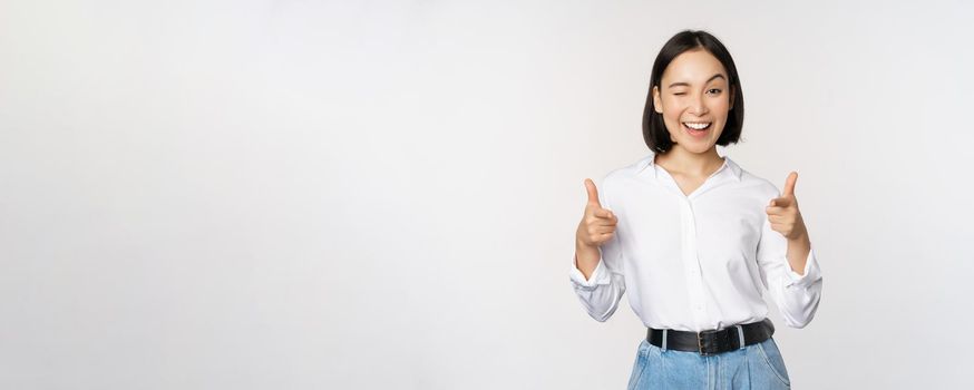 Its you congrats. Smiling attractive asian woman, businesswoman pointing fingers at camera with pleased face, complimenting, inviting you, standing over white background.