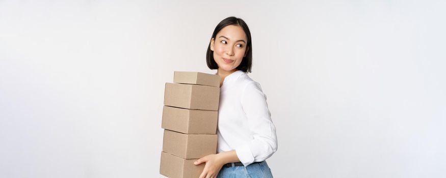 Portrait of young asian woman holding boxes, carry delivery goods. Korean female entrepreneur assemble order, standing voer white background.