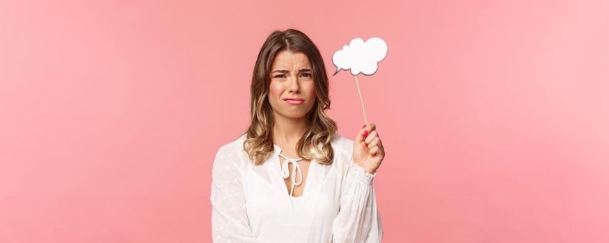 Spring, happiness and celebration concept. Close-up portrait of skeptical and hesitant young blond girl express dislike or reluctance, holding commend cloud stick near head, grimacing disappointed.