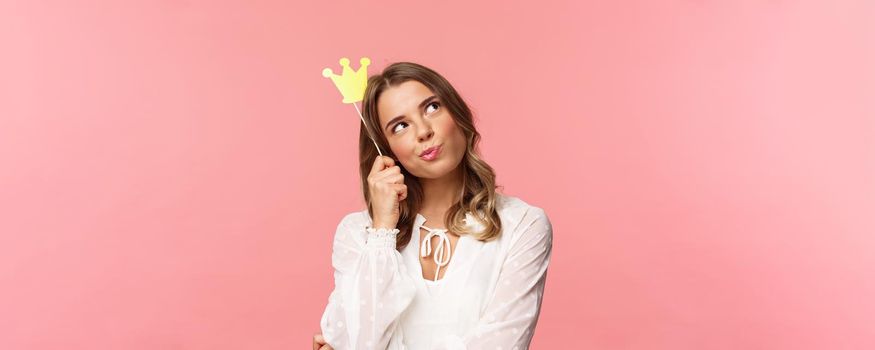 Spring, happiness and celebration concept. Close-up portrait of thoughtful young confident and attractive girl feeling like queen of night party, daydreaming, thinking with crown mask on head.