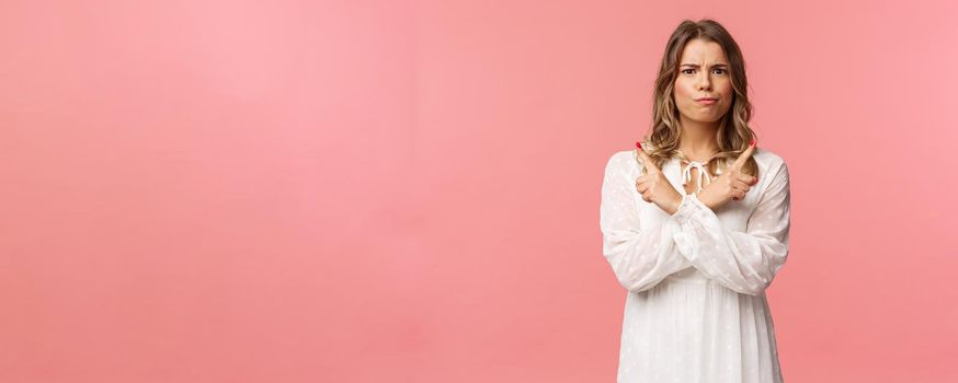 Beauty, fashion and women concept. Portrait of troubled blond girl in white dress need advice, trying make choice, smirk and frown puzzled, pointing left and right two variants, pink background.