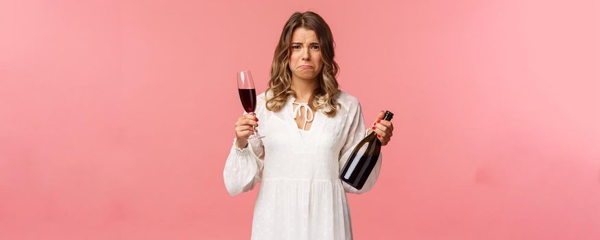 Holidays, spring and party concept. Portrait of upset and whining young blond woman being cheated trying to ease pain with alcohol, holding glass wine and bottle, grimacing want cry, complaining.