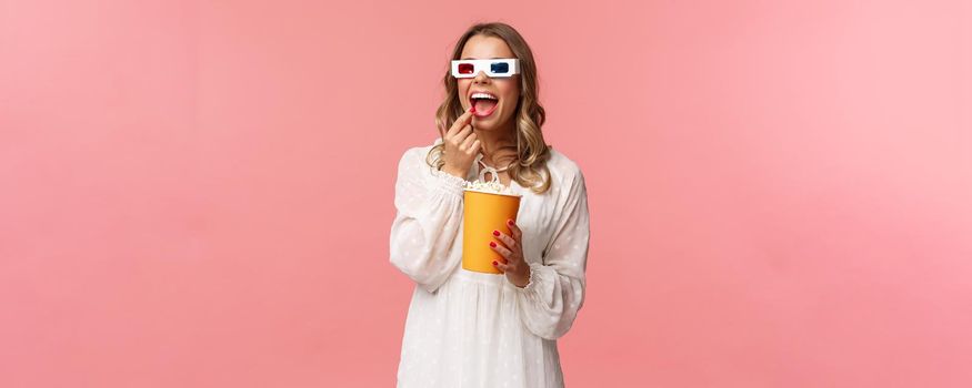 Leisure, going-out and spring concept. Portrait of attractive young woman in white dress enjoying watching interesting movie on full screen at cinema, eating popcorn and wearing 3d glasses.