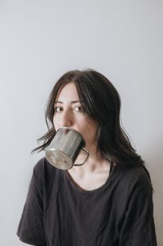 Young woman with a cup of tea at the window during quarantine wearing face mask worried about the new lifestyle. Anxiety, stress, mental health, crisis, depression, psychology therapy.