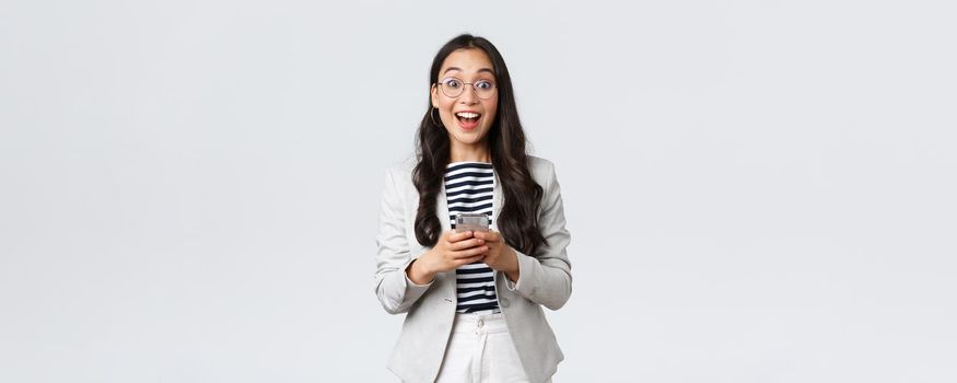 Business, finance and employment, female successful entrepreneurs concept. Cheerful happy asian businesswoman, office manager looking upbeat camera with smile, using smartphone.
