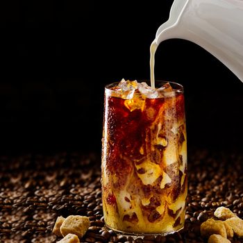 Tasty Iced coffee. Tasty ice coffee with milk, cold drink in glass with ice on dark coffee background Copy space.