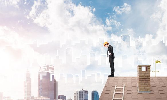 Young businessman in suit and helmet on roof edge. Mixed media