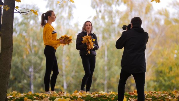 Acrobatic girls posing in front of the photographer, holding yellow and orange leaves. Autumn