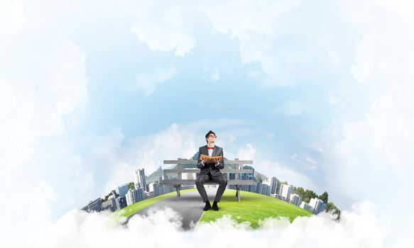 young student sits on a bench with a book in his hands