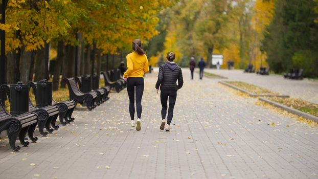 Young fit women running in autumn park. Back view