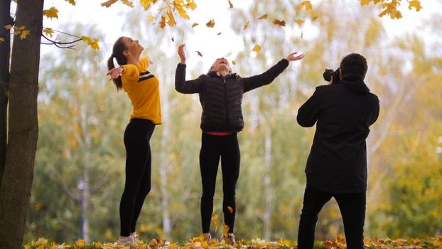 Acrobatic girls posing in front of the photographer, throwing in the air yellow and orange leaves. Autumn