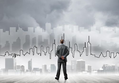 Businessman standing with back and looking at silhouette of modern business center