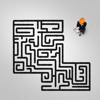 Top view of puzzled businesswoman in helmet looking at drawn maze on floor