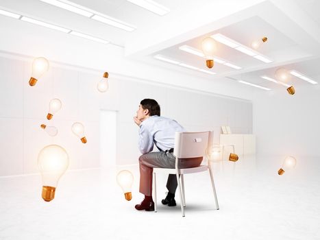 young businessman sits on an office chair. thoughtful and looking up. ideas fly around