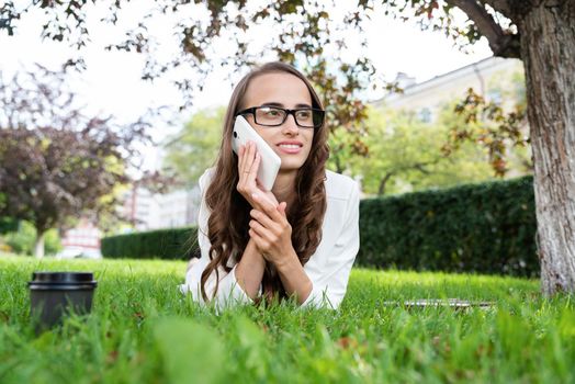 A portrait of a smiling beautiful woman talking on the phone, lying on the lawn
