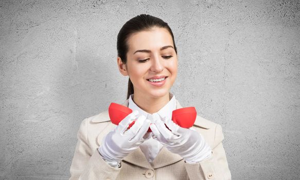 Smiling young woman holding retro red phone. Call center operator in white business suit posing with phone in hands. Hotline telemarketing concept. Professional business assistance and consultation.