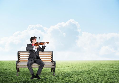 a young businessman plays the violin. sits on a wooden bench. Concept of Creativity in Business