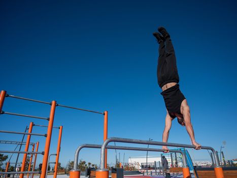 Shirtless man doing handstand on parallel bars at sports ground
