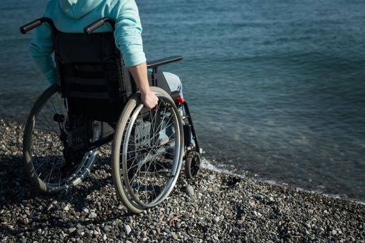 Caucasian woman in a wheelchair on the seashore. Close-up of female hands