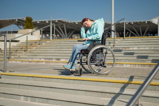 A caucasian woman in a wheelchair cannot go down stairs without a ramp. Hard to access environment