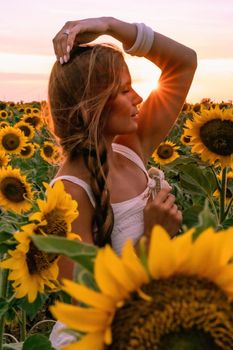 Beautiful middle aged woman looks good in a hat enjoying nature in a field of sunflowers at sunset. Summer. Attractive brunette with long healthy hair