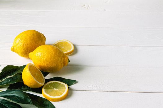 fresh sliced lemon with green leaves on white wooden natural background. Space for text