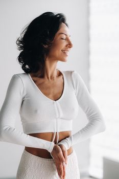 a female yogi in white clothes stands with her hands clasped at the bottom meditating in the yoga hall.