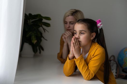 Religious Christian girl and her mother praying at home.