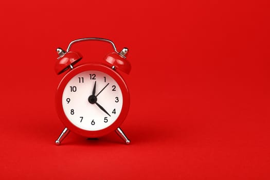 Close up one small red metal twin bell retro alarm clock over red paper background with copy space, low angle front view