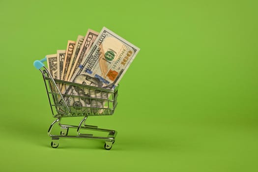 Close up several different value US dollar paper currency banknotes in small shopping cart over green background, low angle side view