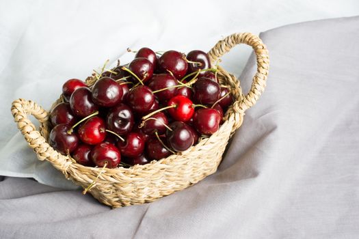 wicker basket full of cherries with textile background in white and gray tones