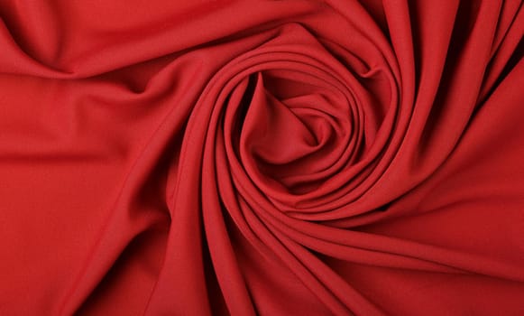 Close up abstract textile background of spiral shaped red folded pleats of fabric, elevated top view, directly above
