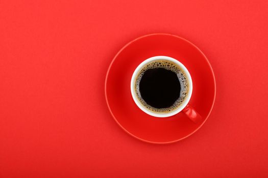 One full morning Americano black coffee with froth edge in small red cup with saucer on red paper background, top view, bird eye view