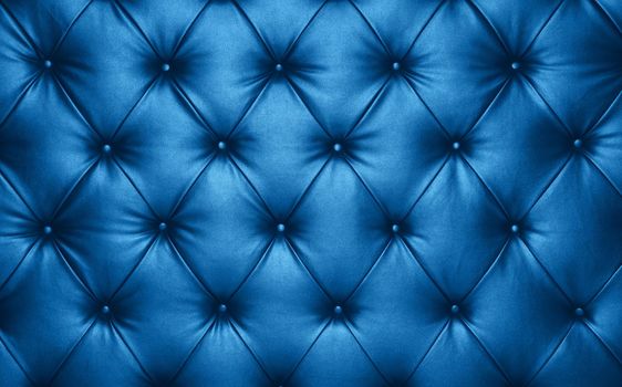 Close up background texture of dark blue capitone genuine leather, classic retro Chesterfield style soft tufted furniture upholstery with deep diamond pattern and buttons