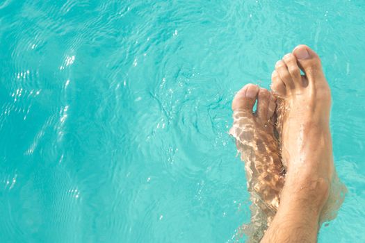 pretty man's feet in the turquoise blue pool water horizontal background