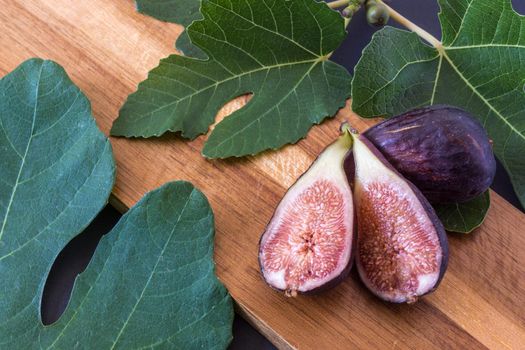 fresh cut figs on a brown wooden board surrounded by fig leaves in landscape format with natural lighting